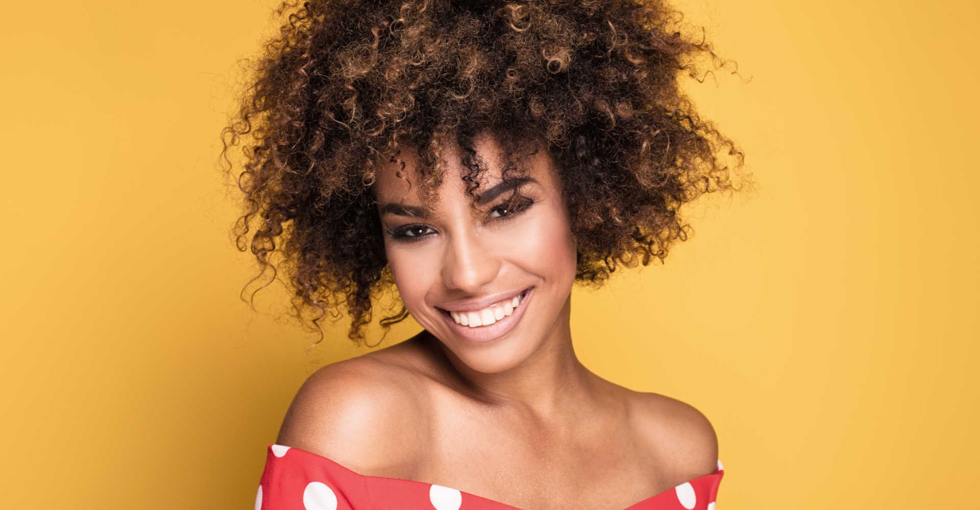 Modelo negra sorrindo com cabelos cacheados